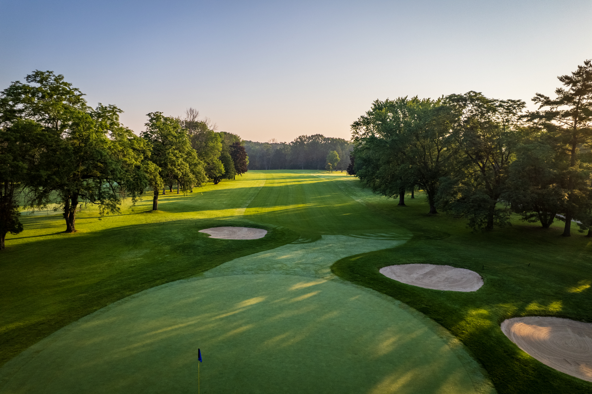 De Pere Water Tower golf course — fairway view down a tree-lined hole with bunkers at sunrise