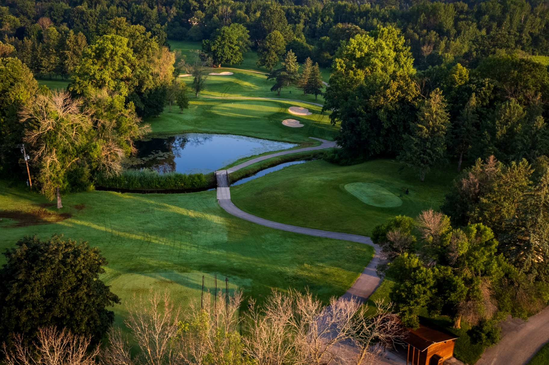 De Pere Water Tower golf course — aerial view of pond, bridge, and bunkered green at golden hour